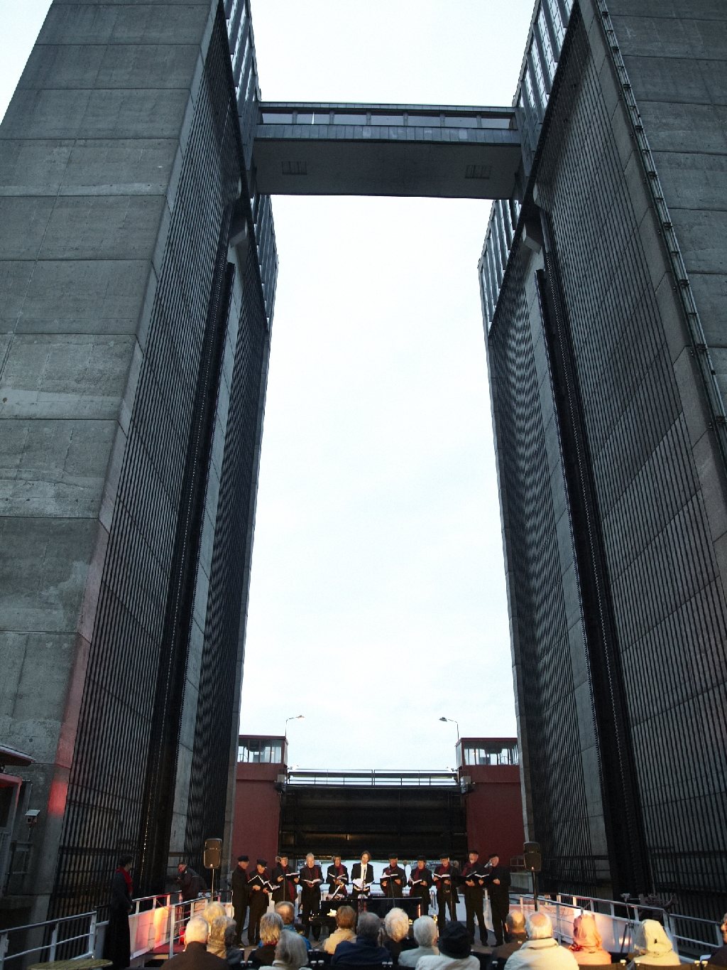 Ein Chor singt am Bug eines Flussschiffes im Trog des Schiffshebewerks Scharnebeck, zwischen den hohen Betontürmen, davor das Publikum
