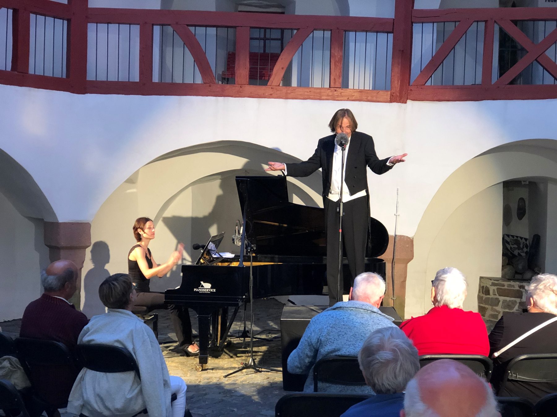 Ein Sänger im Frack breitet im Burghof die Arme aus, am Flügel eine Pianistin, davor Zuhörer