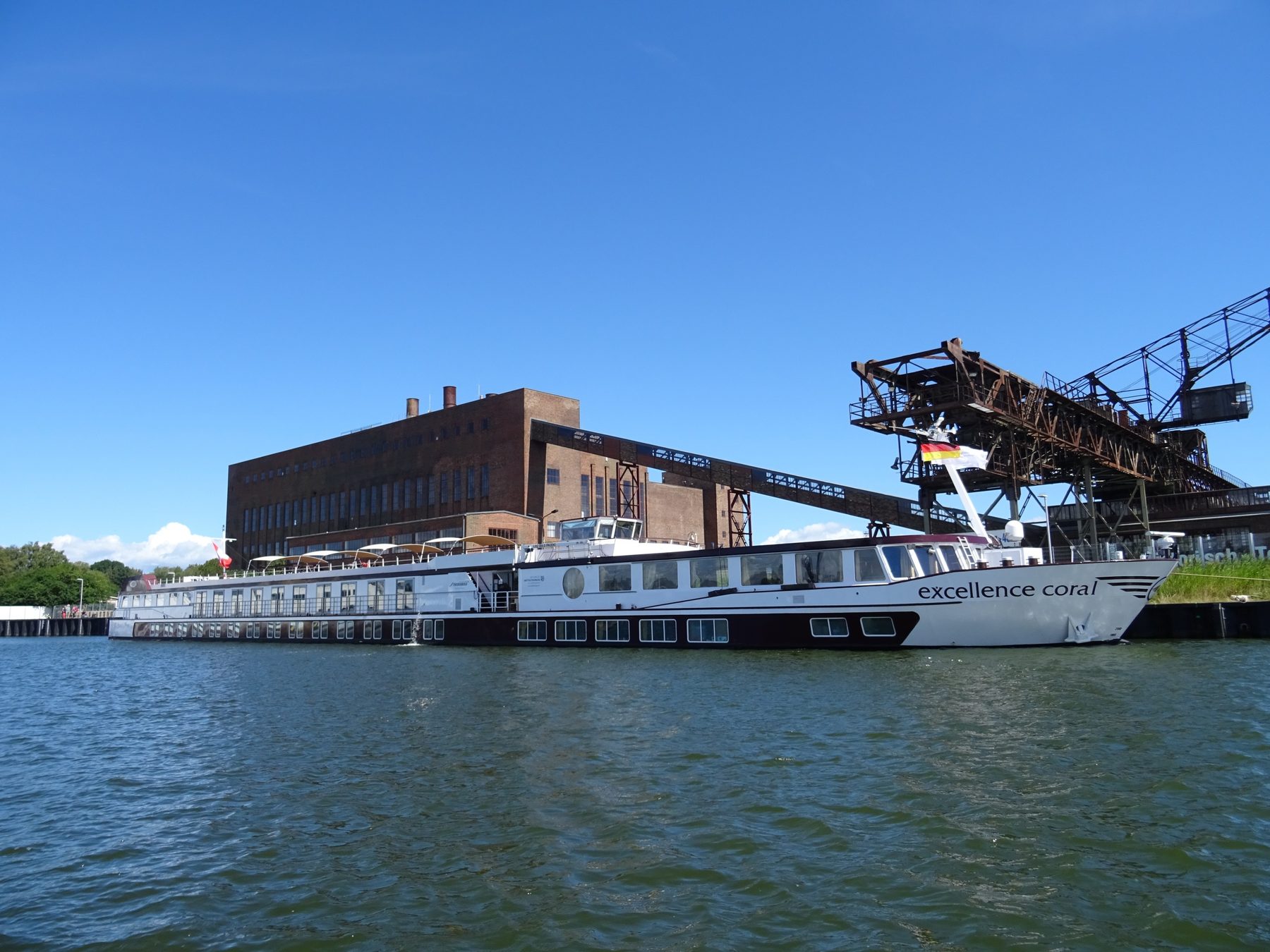 Das Flussschiff Excellence Coral am Kai vor dem Kraftwerksgebäude des Museums Peenemünde
