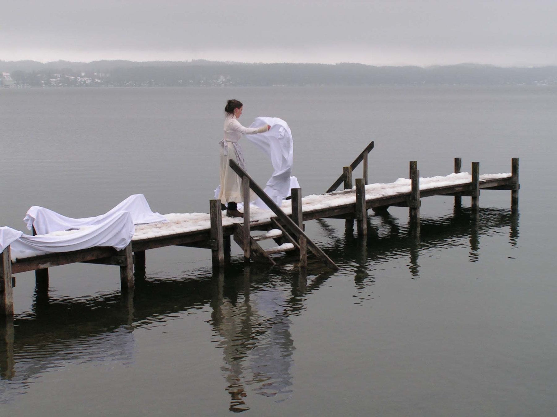 Eine Frau in Weiß auf einem Steg am See im Winternebel