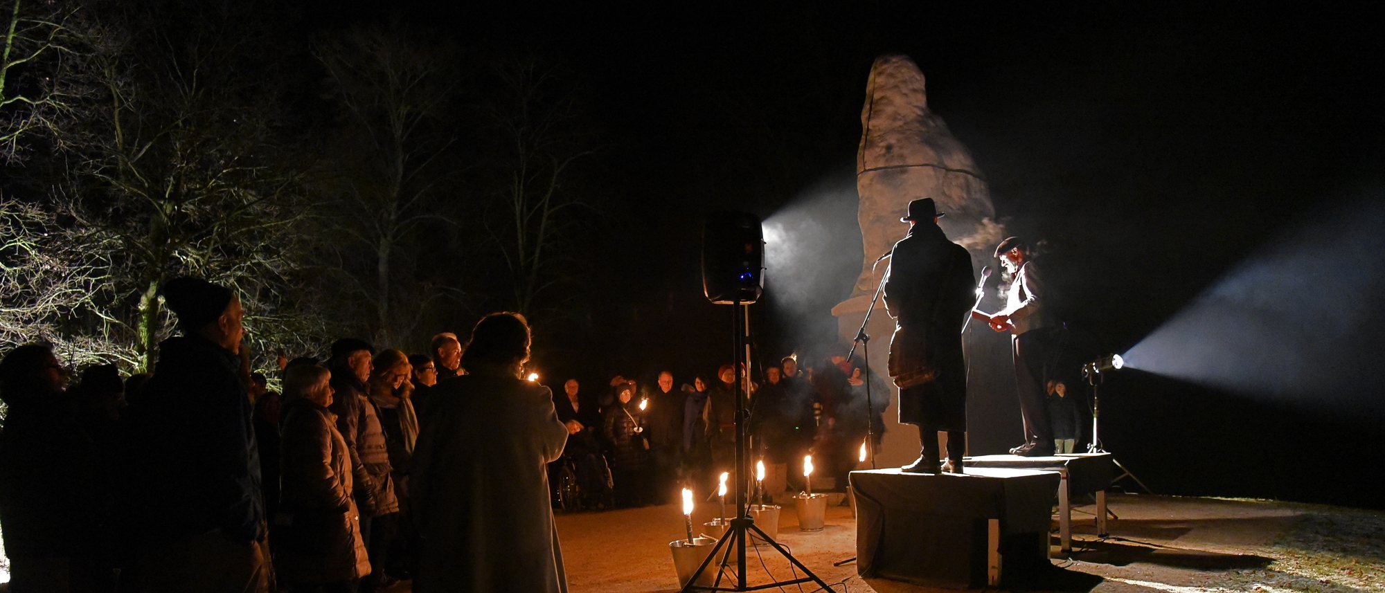 Nachts im Schlosspark: Darsteller auf einem kleinen Podest vor einer Statue im Scheinwerferlicht, davor stehendes Publikum und Kerzen am Boden